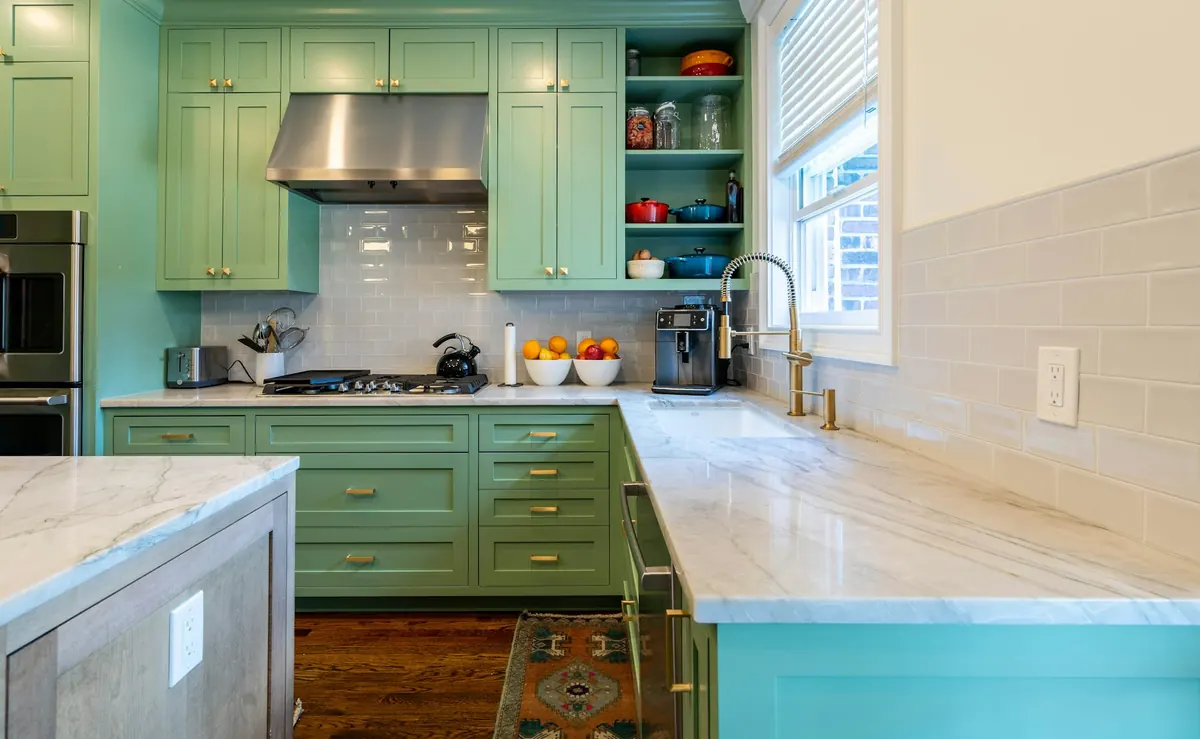 A kitchen with sage green shaker cabinets, brass hardware and marble counters