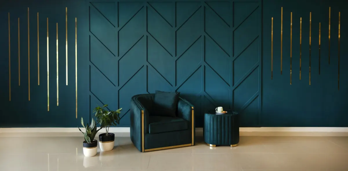 A deep teal painted feature wall with chevron panelling behind a velvet armchair in a bright lounge