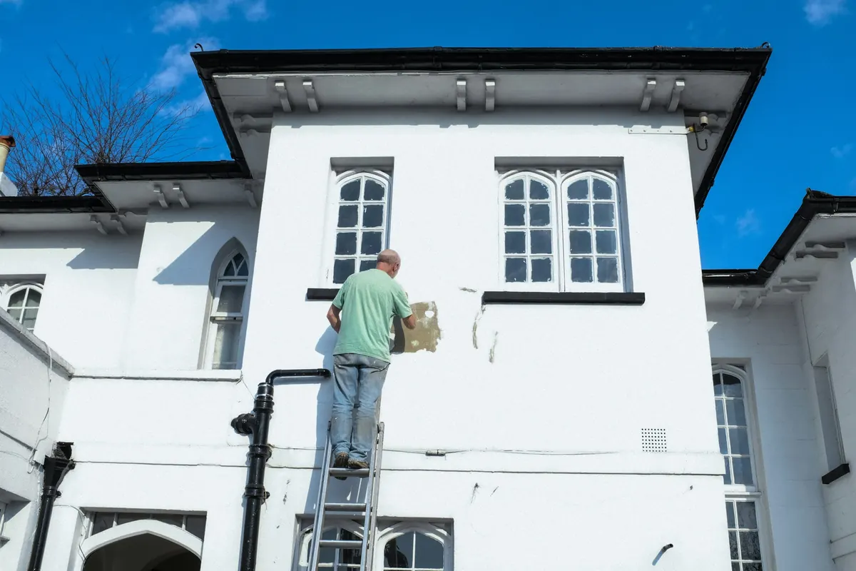 A painter on a ladder touching up the white exterior of a two-storey house