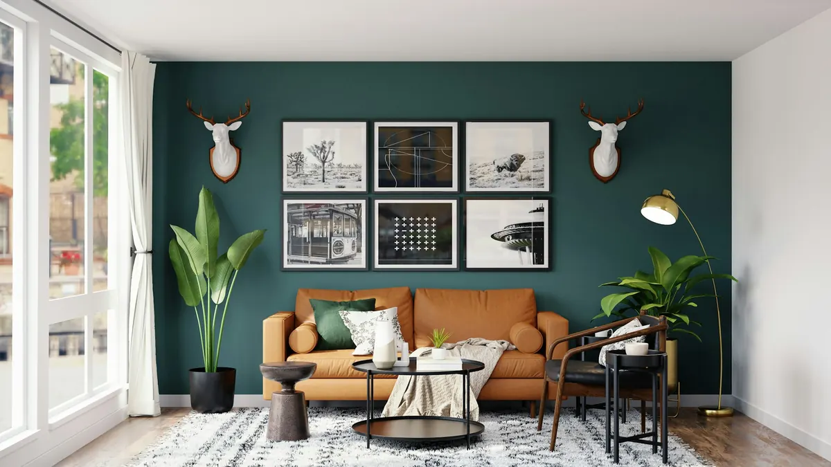 A living room with a deep green accent wall, framed prints and a tan leather sofa