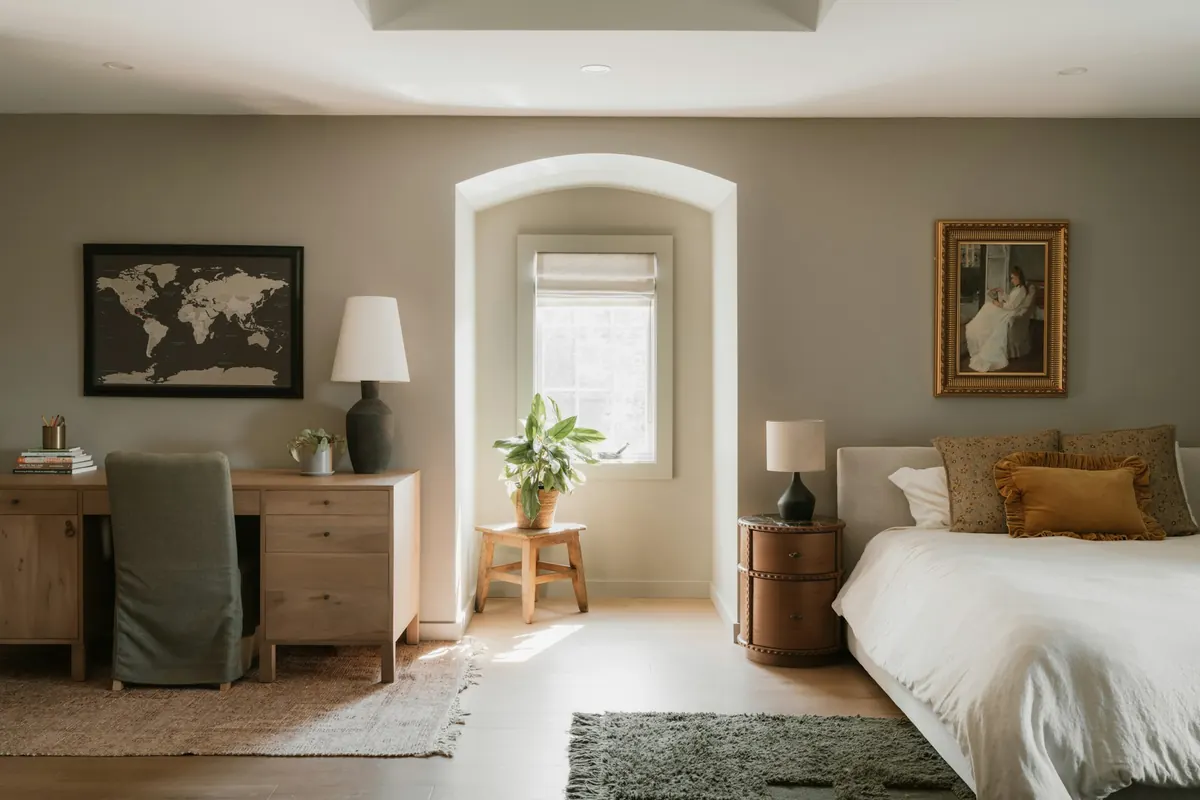 A sunlit bedroom with soft greige walls, an arched window alcove and a white linen bed