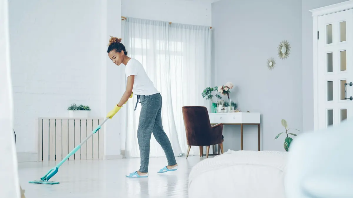 A cleaner in yellow rubber gloves mopping the glossy white floor of a bright room