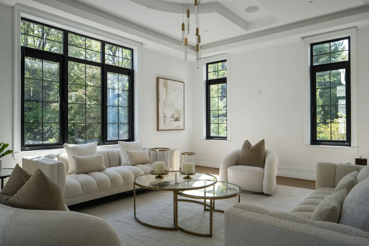 A cream living room with bouclé sofas, a glass-and-brass coffee table and large black-framed windows