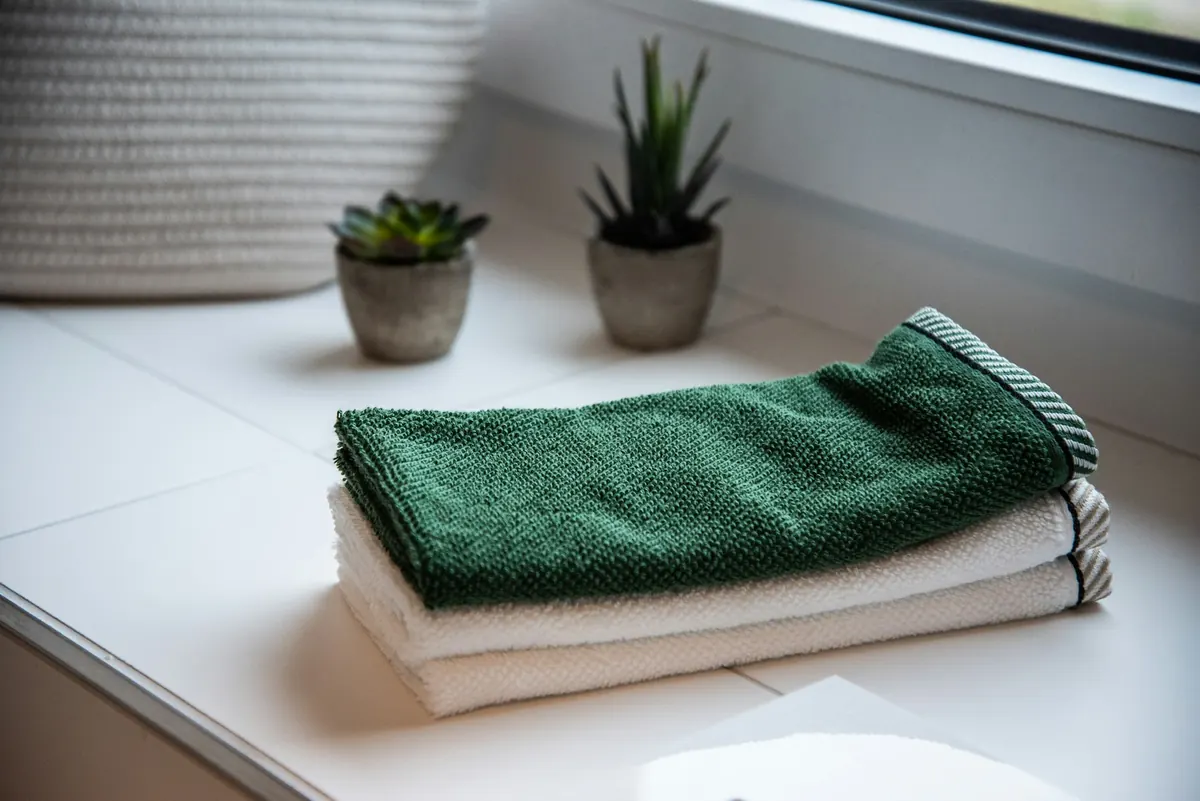 Neatly folded green and white hand towels on a white windowsill beside two small succulents