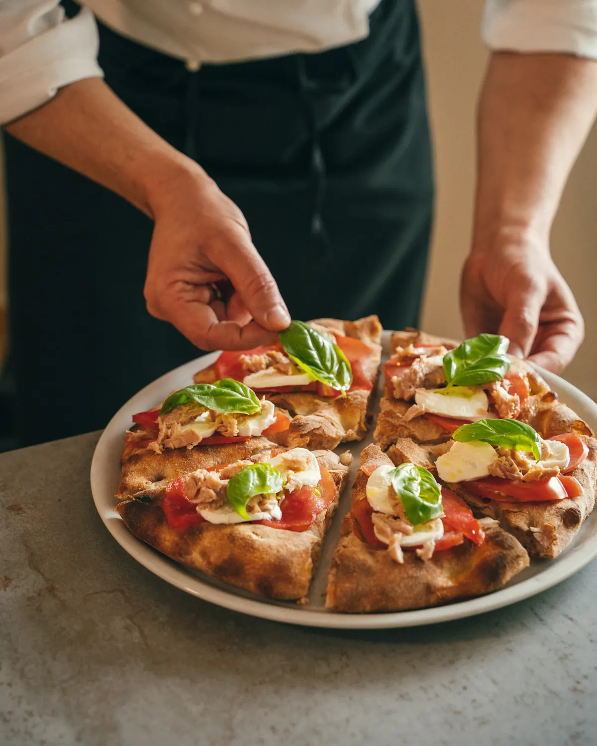 A chef placing basil leaves on a freshly sliced pizza