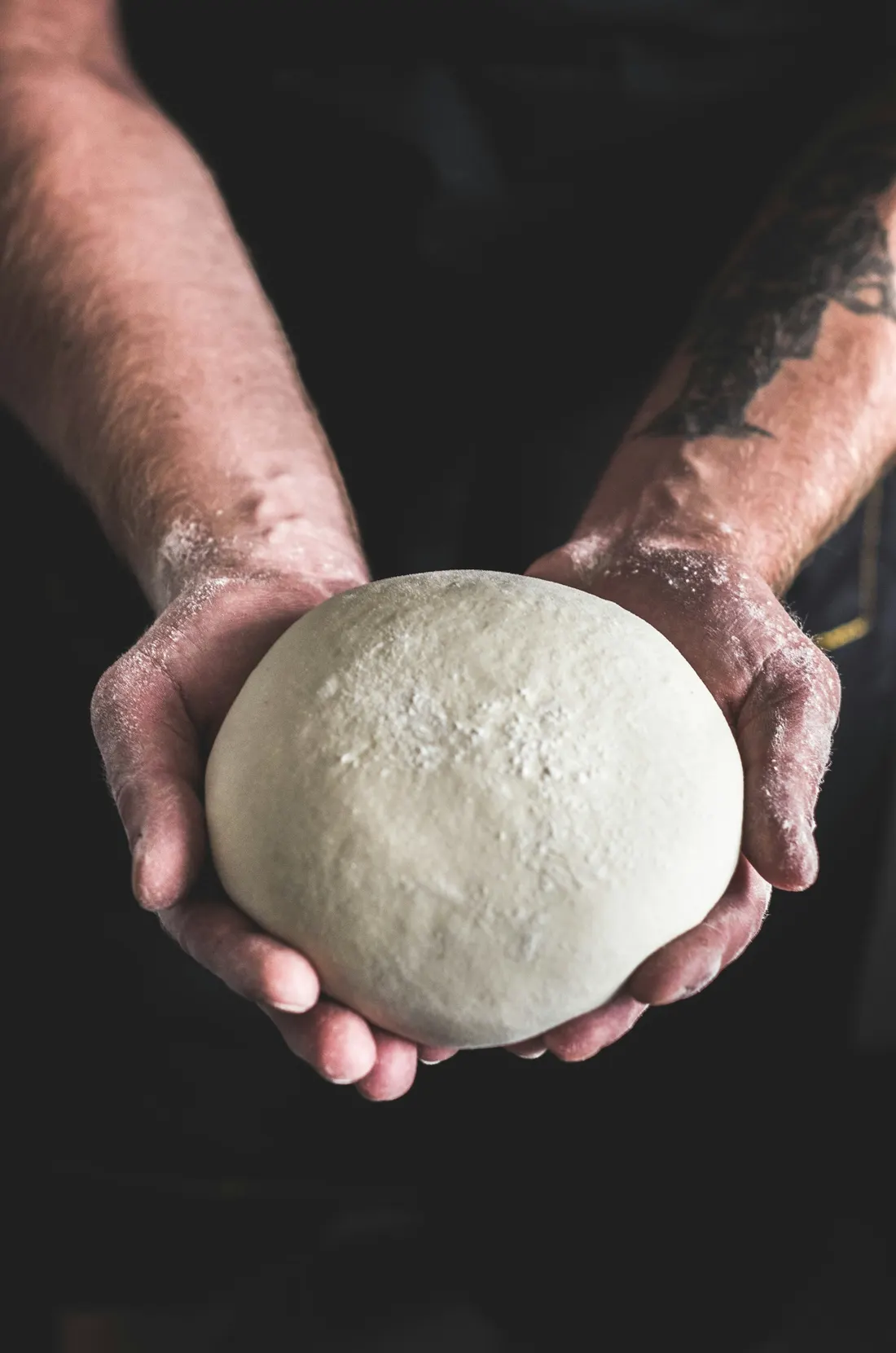 Floured hands holding a smooth ball of pizza dough
