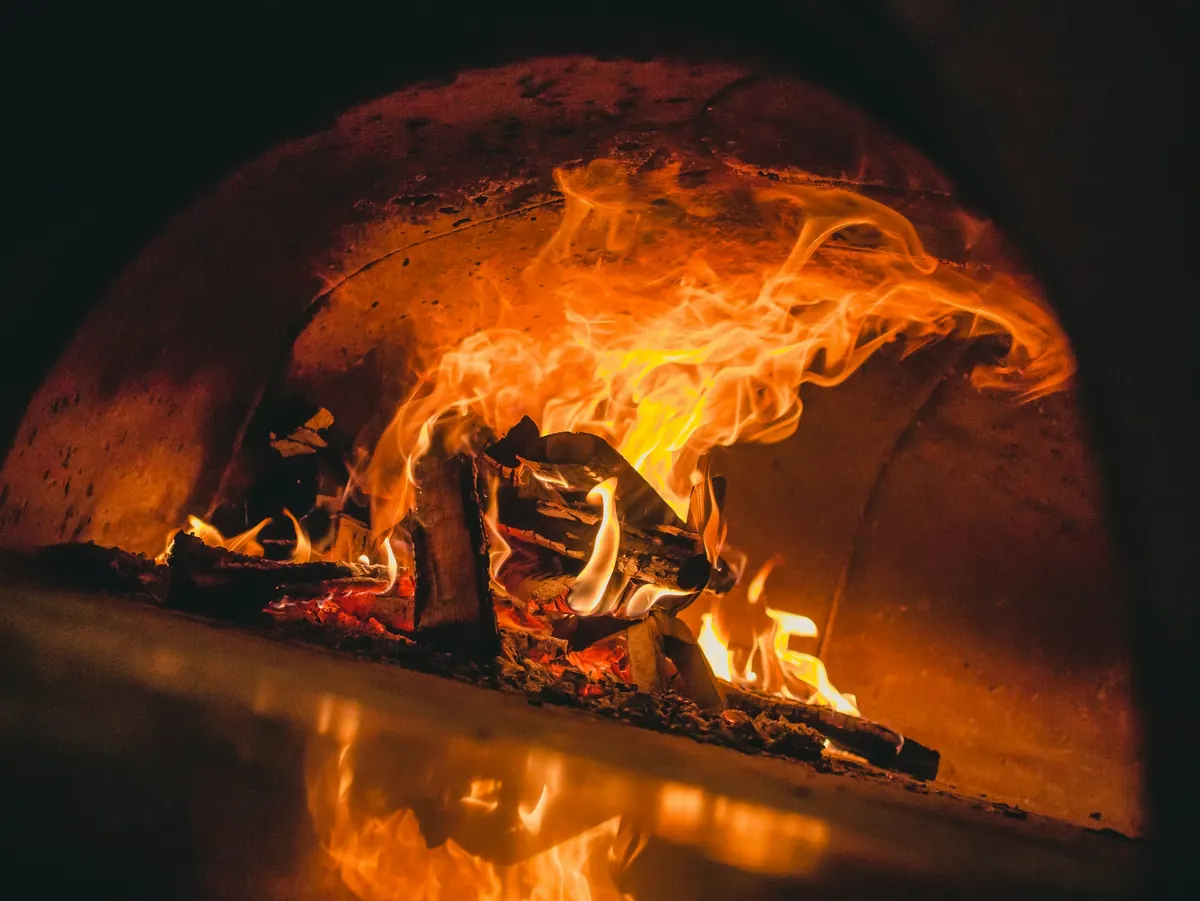 Flames curling up the domed brick ceiling of a wood-fired oven over burning logs
