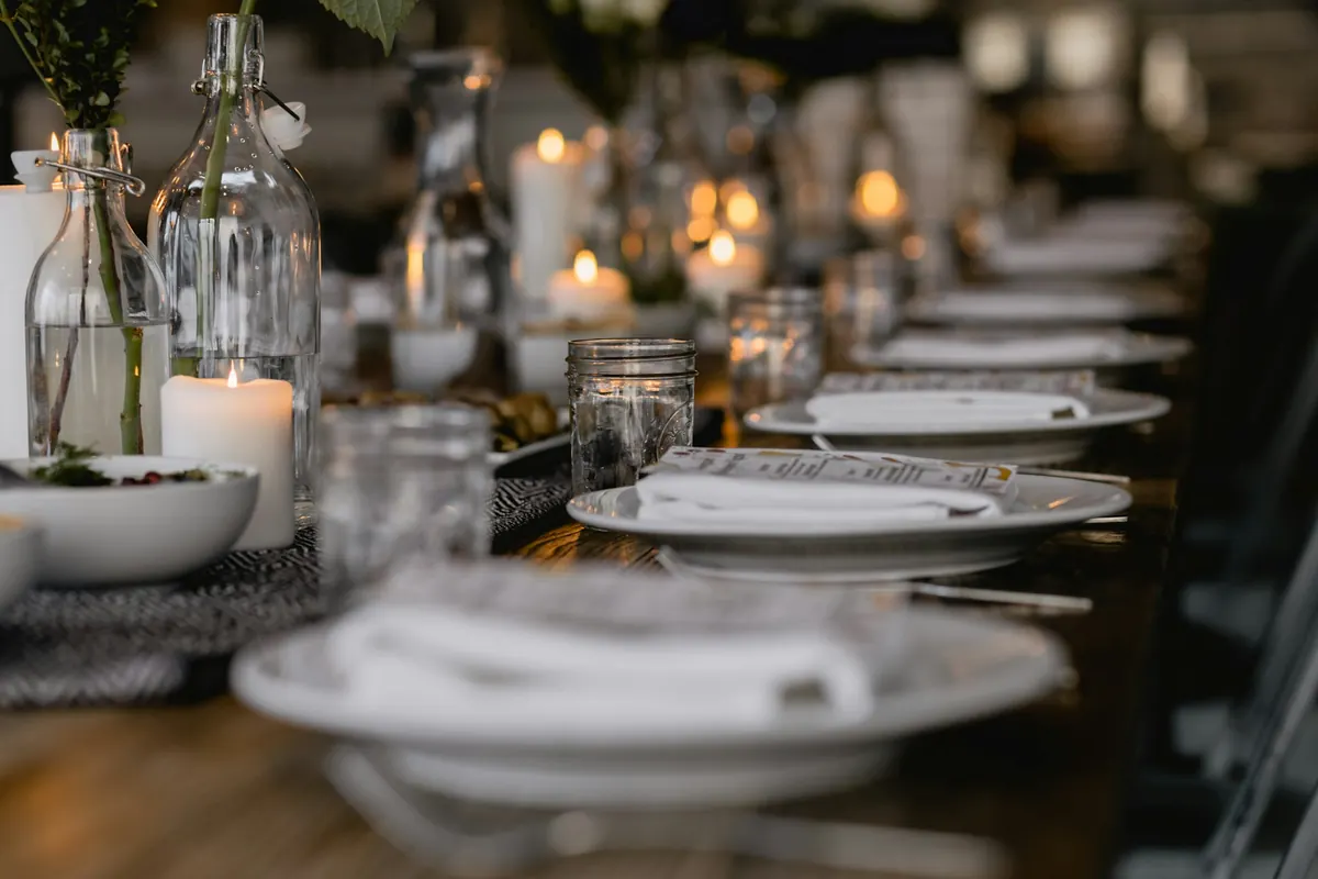 A long table set for a group with white plates, folded napkins and lit candles