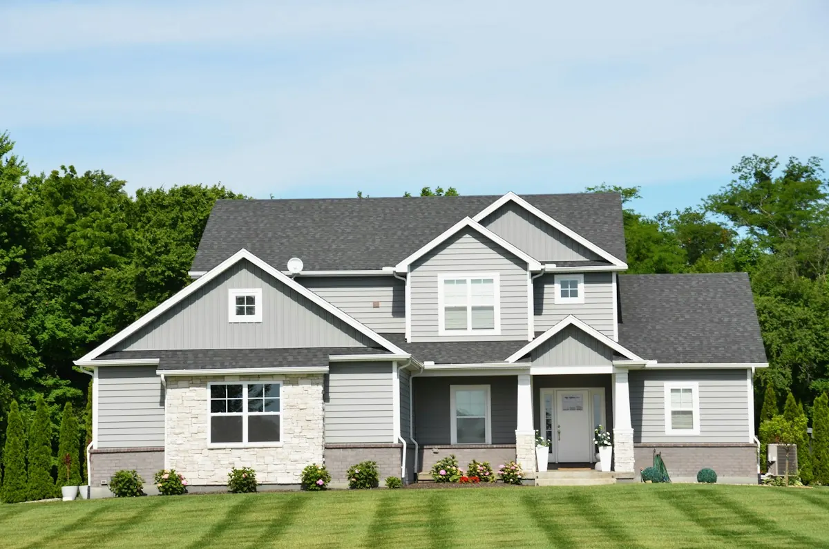 A grey two-storey home with a new shingle roof and a striped lawn