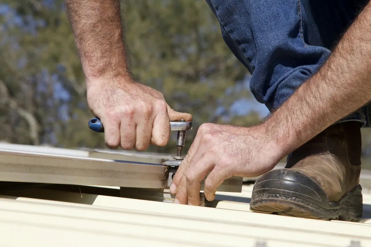 A roofer fastening a metal roof panel with a socket wrench